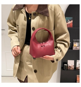 Detail of burgundy leather handbag featuring a curved silhouette and dual zippers