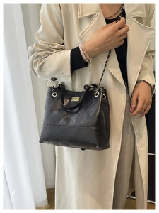 Close-up of black quilted bucket bag with gold clasp and leather chain strap on a model