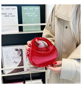 Detail of red acrylic chain bag with striped texture and round handle held by a model