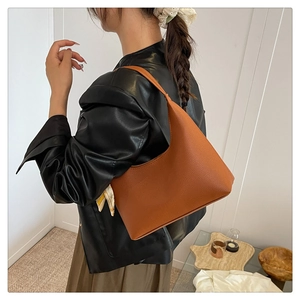 Detail of orange pebble leather crescent bag featuring a decorative floral silk scarf