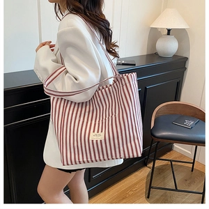 Detail of red and white striped canvas tote bag worn with a white blazer for commute
