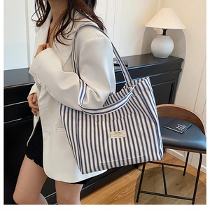Detail of blue and white striped canvas tote bag with woven label on a female model