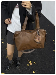 Detail of a brown faux leather tote bag featuring a detachable woven strap and donut charm