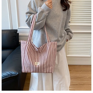 Detail of red striped canvas tote bag with front pocket held by model in modern home