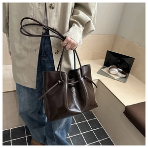 Dettaglio borsa tote in pelle lucida marrone scuro con nodi laterali e manici sottili