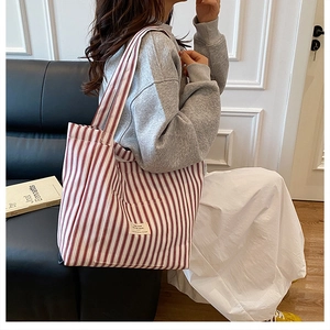 Detail of red and white striped canvas tote bag showing side pocket and woven logo label