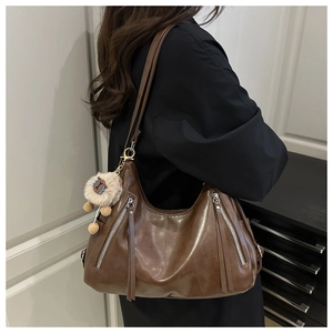 Close-up of deep brown leather tote with silver zippers and plush ball keychain detail