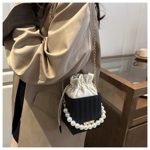Detail of a black woven bucket bag featuring pearl handle and gold chain strap