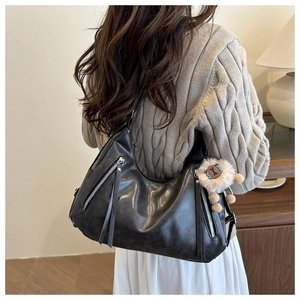 Detail of hobo shoulder bag with silver zippers and a cute plush lion charm on a model