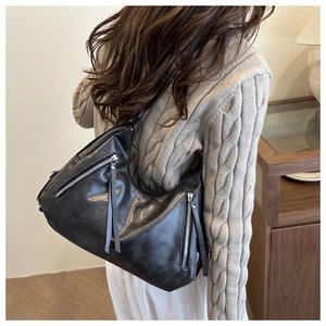 Close-up of black retro leather shoulder bag with silver zippers and long fringe details