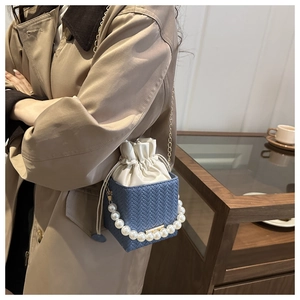 Close-up of navy woven square bag featuring a large pearl handle and gold chain strap