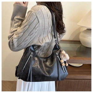 Close-up of black leather tote bag with silver zippers, tassels and a brown plush ball charm