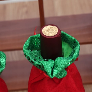 Christmas wine bottle cover with red sequins and green collar on wooden background