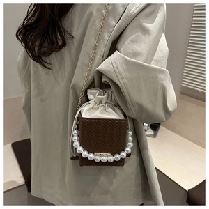 Detail of woven brown bucket bag featuring a large pearl handle and gold chain strap