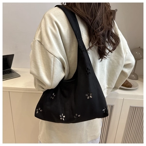 Vue latérale d'un sac hobo noir avec fleurs découpées au laser porté par un mannequin