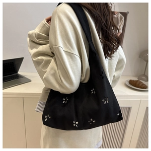 Detail of black suede shoulder bag with laser-cut floral patterns shown on a model
