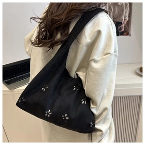 Detail of laser-cut floral patterns on black canvas hobo tote bag worn by model