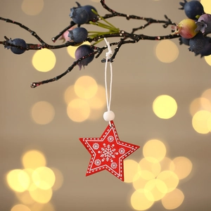 Detail of a red wooden star ornament with snowflake patterns hanging on a pine branch