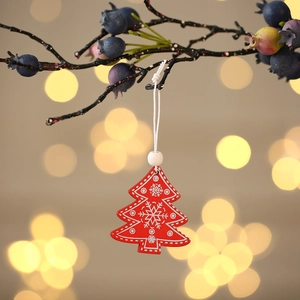 Detail of a red wooden Christmas tree ornament with white snowflake patterns on a branch