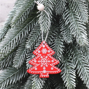 Close-up of red wooden Christmas tree ornament with white snowflakes hanging on pine branches