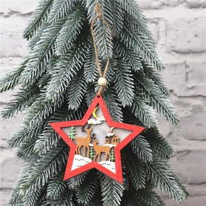 Detail of red wooden star ornament with reindeer and forest scene hanging on pine branch