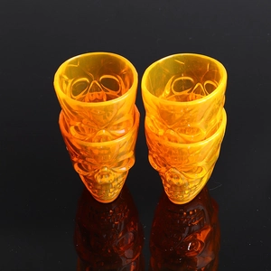 Set of 4 translucent orange skull cups for Halloween decoration on a black reflective base