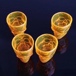 Set of four translucent orange skull-shaped shot glasses for Halloween party decoration