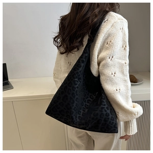 Detail shot of a large black leopard print hobo tote bag worn by a model in a minimalist room