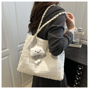 Detail of cream woven tote bag with braided handle and plush cloud charm accessory