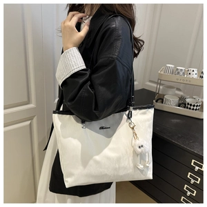 Gros plan d'un sac cabas blanc avec bordure noire et pendentif monstre en peluche