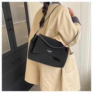 Close-up of black matte leather shoulder bag with chain strap worn by a model