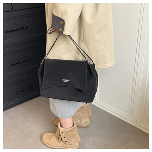 Detail of minimalist black leather underarm bag with metal chain strap and logo