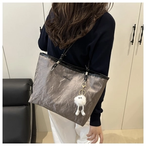 Détail d'un grand sac cabas gris texturé avec sangles noires et pendentif en peluche