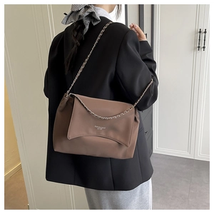 Brown leather crossbody bag with wave-cut flap and silver logo shown on model shoulder