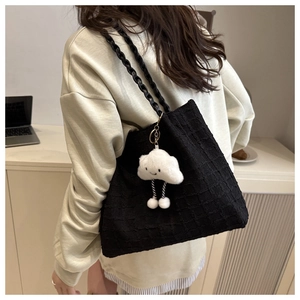 Detail of black checkered tote bag featuring a plush charm and braided shoulder strap