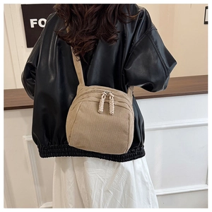 Detail of khaki corduroy crossbody bag with dual rope zippers on a stylish jacket