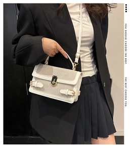 Detail of white textured fabric handbag with gold metal lock and leather stitching
