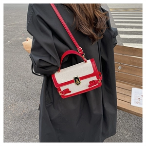 Detail of red and cream canvas crossbody bag worn with a black coat in a street setting
