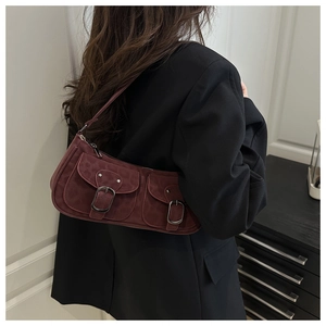 Detail of dark red shoulder bag with dual flap pockets and metallic buckles on textured fabric