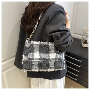 Close-up of black and white tweed crossbody bag with golden chain and fringe details