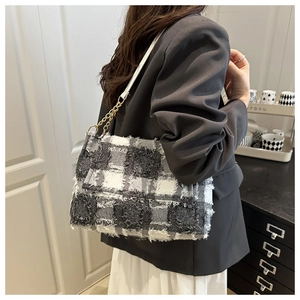 Close-up of black and white tweed shoulder bag with fringe edges and gold chain detail
