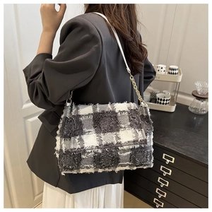Detail view of black and white plaid tweed shoulder bag with metal chain strap on model