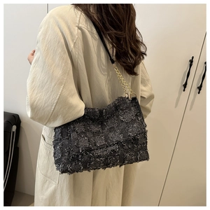 Detail of tweed crossbody bag with gold chain strap worn by a model in a minimalist setting