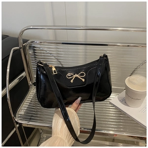 Detalle de bolso de hombro en charol negro con hebilla de lazo dorado y cremallera