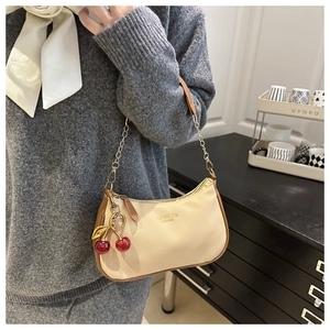 Détail d'un sac à bandoulière en cuir beige grainé avec breloque cerise et chaîne dorée