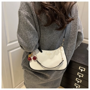Detail of white pebbled leather bag with gold chain and red cherry charm accent