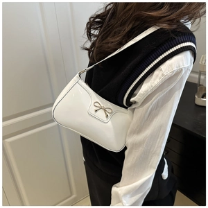 Close-up of white glossy patent leather baguette bag with golden metal bow on a model