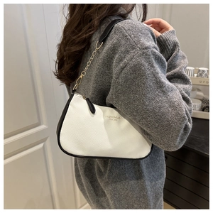 Detail of creamy white crossbody bag with black trim and gold chain shoulder strap