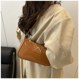 Detail shot of a dark brown patent leather underarm bag with a golden bow knot decoration