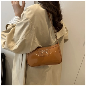 Detail of a brown patent leather underarm bag with a silver metal bow accent